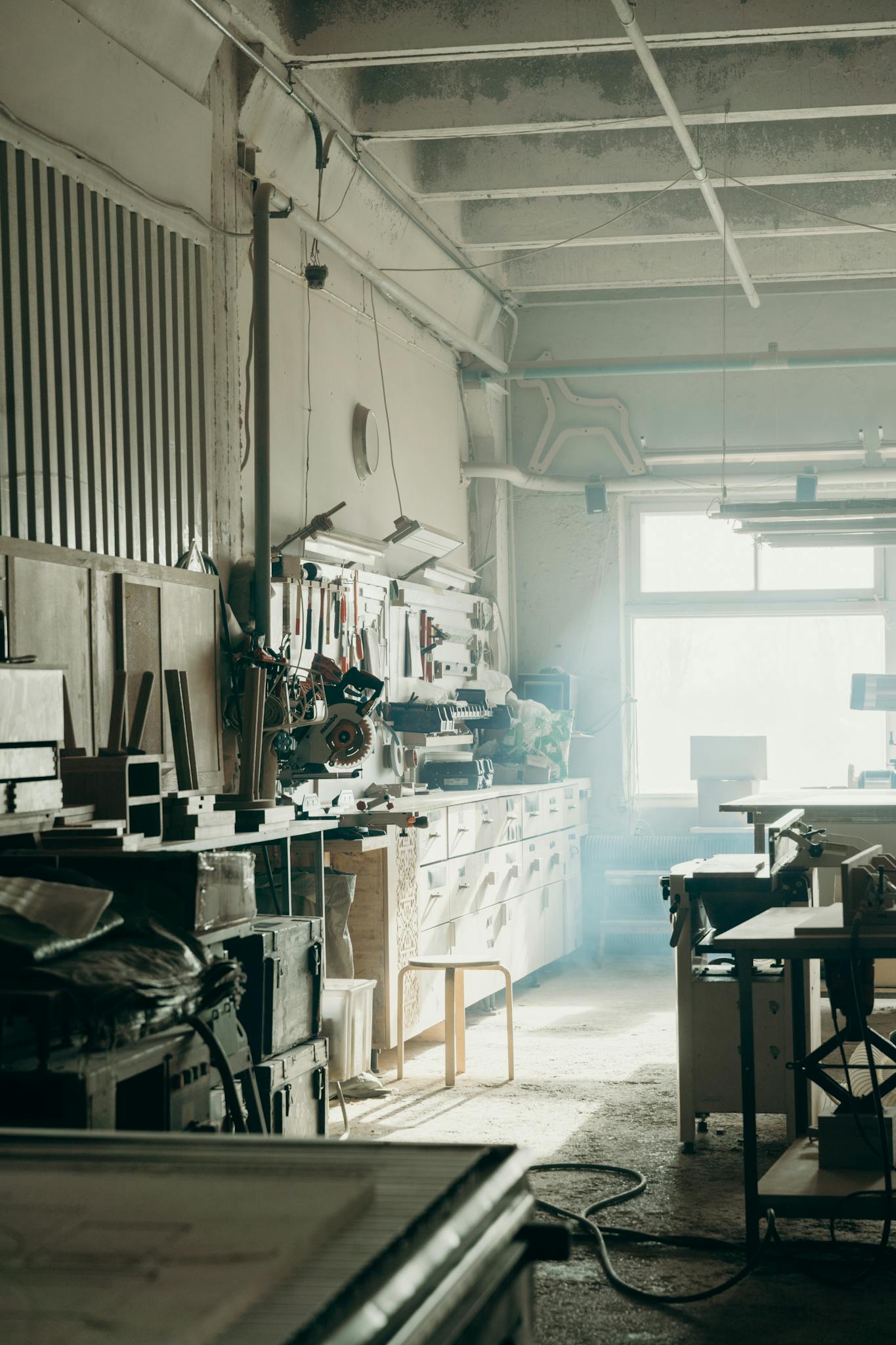 A sunlit industrial workshop with tools and materials scattered around creates a busy and artistic atmosphere.
