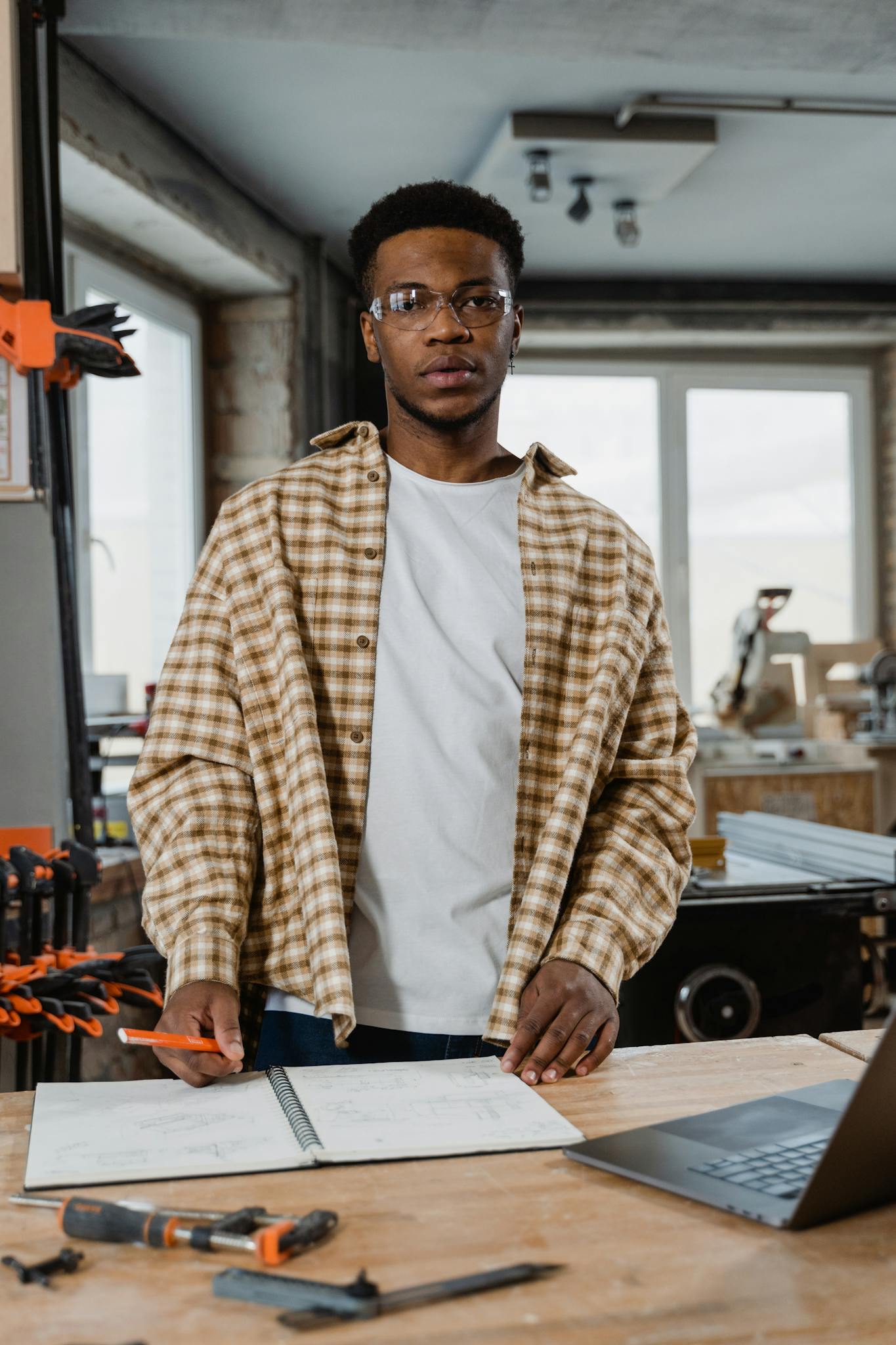 Focused young carpenter planning a woodworking project indoors with tools and plans.
